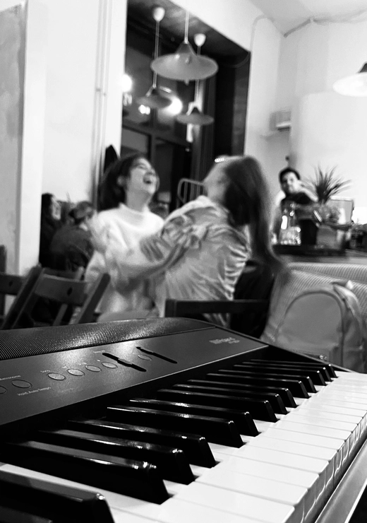 Klawiatura pianina w kawiarni a w tle dwie dziewczyny pełne spontaniczności i radości siedzą przy stoliku razem spędzając dobrze czas
